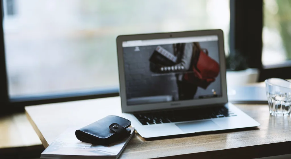 Stock photograph: an open laptop on a wooden desk beside a glass of water, with daylight coming through a window behind it
